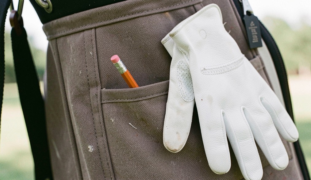 Kort potlood gestoken in het weefsel van een golftasvak naast een opgevouwen witte handschoen